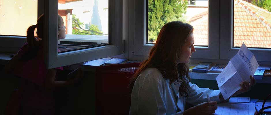 A little girl looks out the window of the examination room while Dr. Paulina Miletić-Simić works. | Mlada jevojčica gleda kroz prozor ordinacije dok Dr. Paulina Miletić-Simić radi.